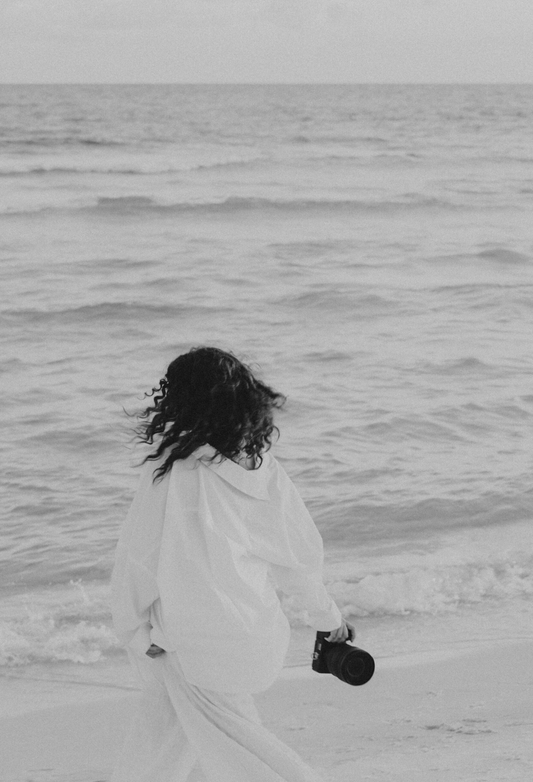 Girl running with camera on the beach.